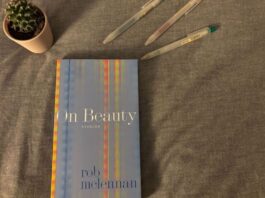 A blue book with the title "On Beauty" by Rob McLennan sits on a bed. Above it is a cactus and three Muji pens. The backdrop is a gray blanket.