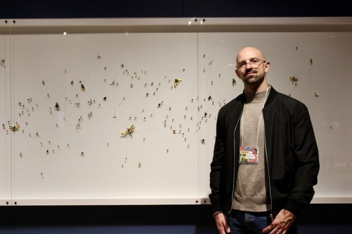 A man stands in front of a display of little green bugs on a white board. 