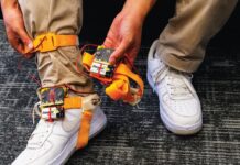 ‘Tap-tap device’ makes non-verbal cues accessible for blind and low-vision musicians Someone wearing brown pants and white air force ones, has a tap tap device strapped to his ankle. The device has orange straps that go around the bottom of the foot and the ankle. The person shows off the battery pack and the device in one of their hands.