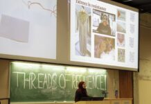 Tatreez combines Palestinian history, artistry and resistance Behind a chalk board with the words "Threads of Resilience" a woman stands. On a projector above her head shows tatreez as resilience and an example of what the embroidery looks like.