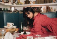 Q&A: Singer-songwriter Zeelle on growing up and finding musical inspiration Laying on a table with teacups and cards, a person in a red dress stares directly at the camera.