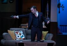 Review: Ottawa Little Theatre’s ‘Guilty Conscience’ is full of suspense and intrigue On stage, a man in a black suit points a gun to someone off stage.