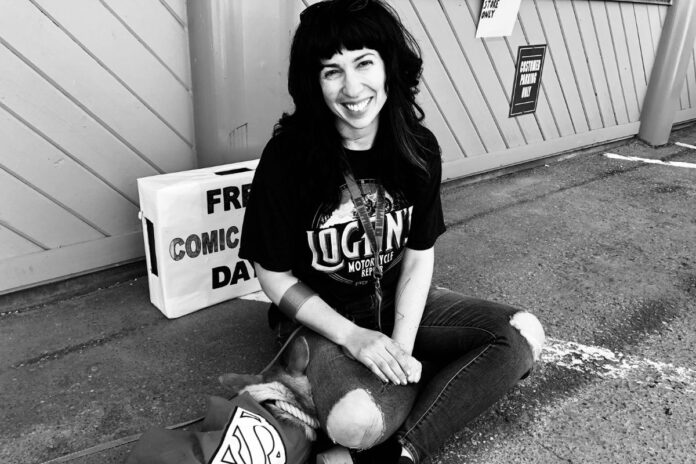 A woman wearing ripped jeans and a black tshirt sits outside an old comic shop, Happy Harbor Comics, in Edmonton on Free Comic Book Day in 2018.