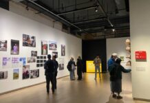 SAW Centre unveils new exhibit addressing homelessness, housing insecurity In a large art gallery, people look at photos of art on the wall.