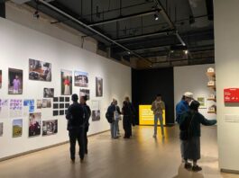 In a large art gallery, people look at photos of art on the wall.