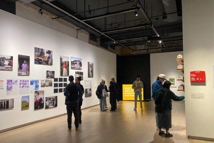 In a large art gallery, people look at photos of art on the wall.