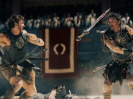 Paul Mescal and Pedro Pascal battle it out in 'Gladiator II.' Pedro throws his sword at Paul, and Paul is mid swing back. They are both wearing Roman gladiator armour and skirts.