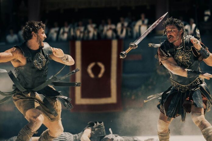 Paul Mescal and Pedro Pascal battle it out in 'Gladiator II.' Pedro throws his sword at Paul, and Paul is mid swing back. They are both wearing Roman gladiator armour and skirts.