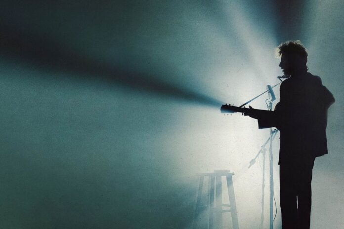 A black silhouette of a artist playing a guitar amid blue stage lighting.