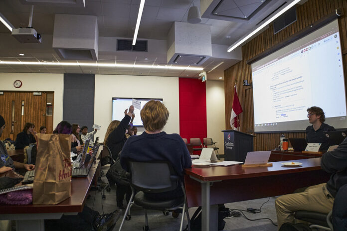 Students in chairs facing a podium at the front of the room.