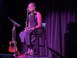 Black woman sits on stool on stage