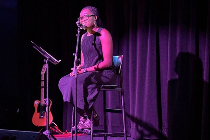 Black woman sits on stool on stage