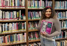 Q&A: Val Hussain discusses Carleton’s queer library, the importance of safeguarding queer media Person holds a book in front of a queer library