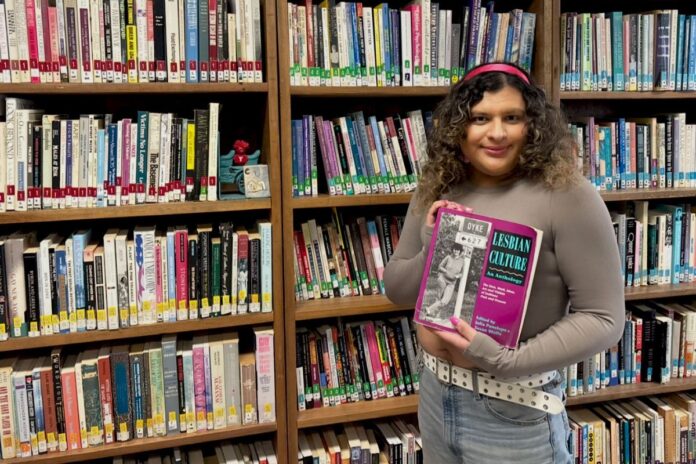 Person holds a book in front of a queer library