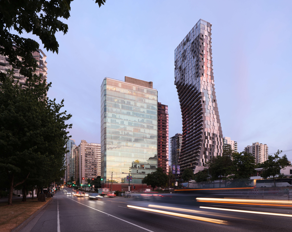 Two tall skyscrapers in downtown Vancouver stand against the dusk, light blue sky.