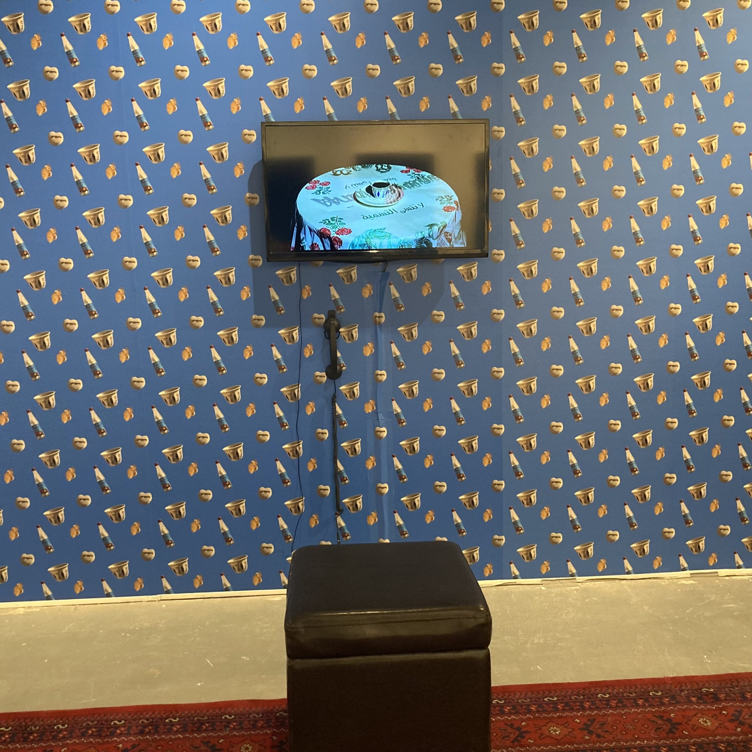 blessings-film-1 A television with a landline phone hanging from the bottom is mounted on a blue wallpapered wall, behind a black stool sitting on the floor.