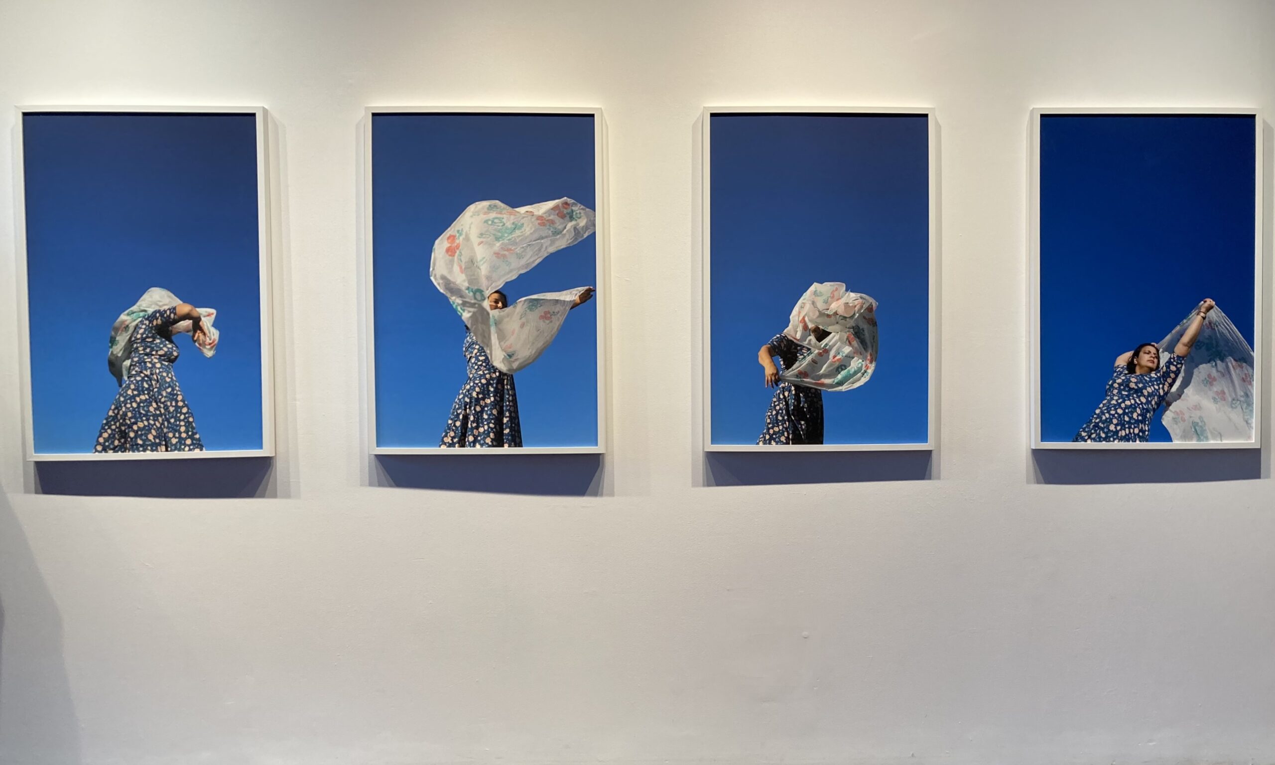 blessings-photos Four photographs of a woman with a tablecloth against a bright blue sky are mounted on a beige wall.