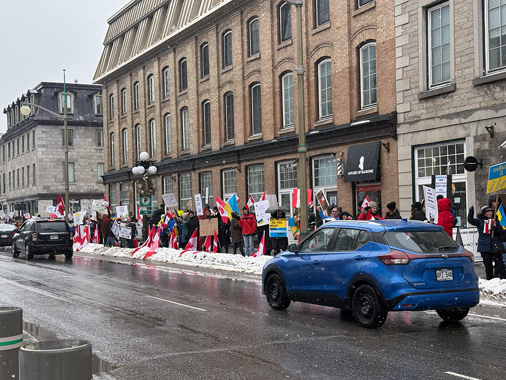 Cars drive by protesters supporting Ukraine in the winter months of downtown Ottawa.