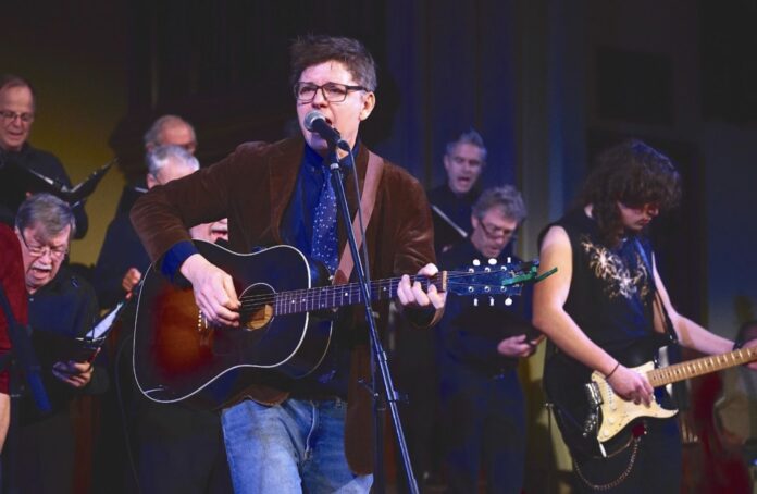 A band performs on a stage, the lead singer has a guitar and microphone.