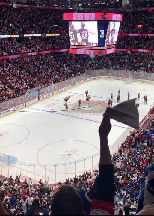 A hockey arena full of people watch a hockey game.