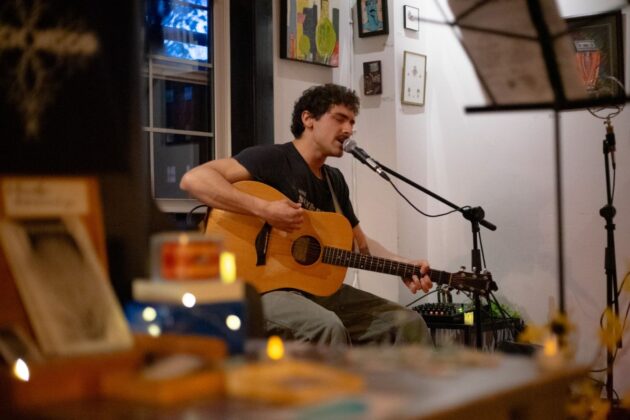 A person sits with a guitar behind a mic stand while performing in a café.