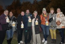 Group of people stand together in the night time holding candles.