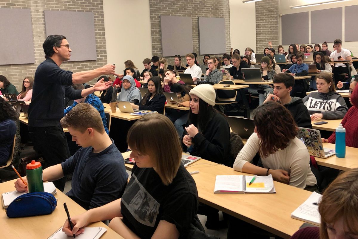 A professor stands and lectures a university classroom full of students.