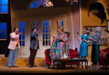 Five people stand on a stage with soft lighting and living room furniture.