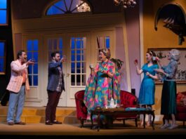 Five people stand on a stage with soft lighting and living room furniture.