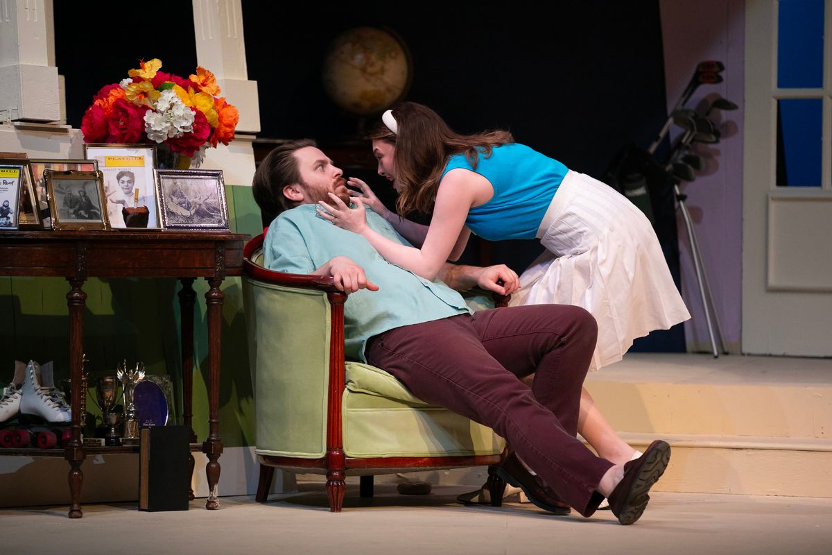 A man sits back in a chair in fear as a woman leans over him.