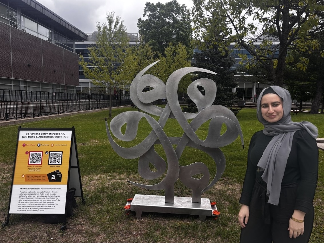 A person stands in front of a calligraphy-inspired sculture in a field. A sign with a QR code sits beside her. 
