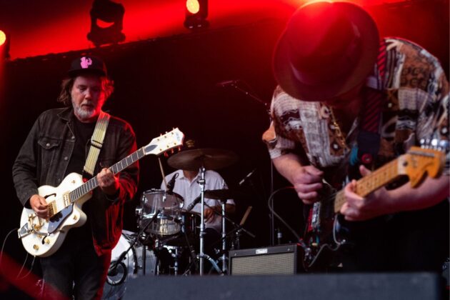 Two guitarists play on stage in red lighting.