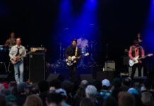 Review: Broken Social Scene’s intoxicating sonic soundscape transforms Ottawa Jazz Festival A band with guitars, drums and other instruments stand on a stage backlit with blue.