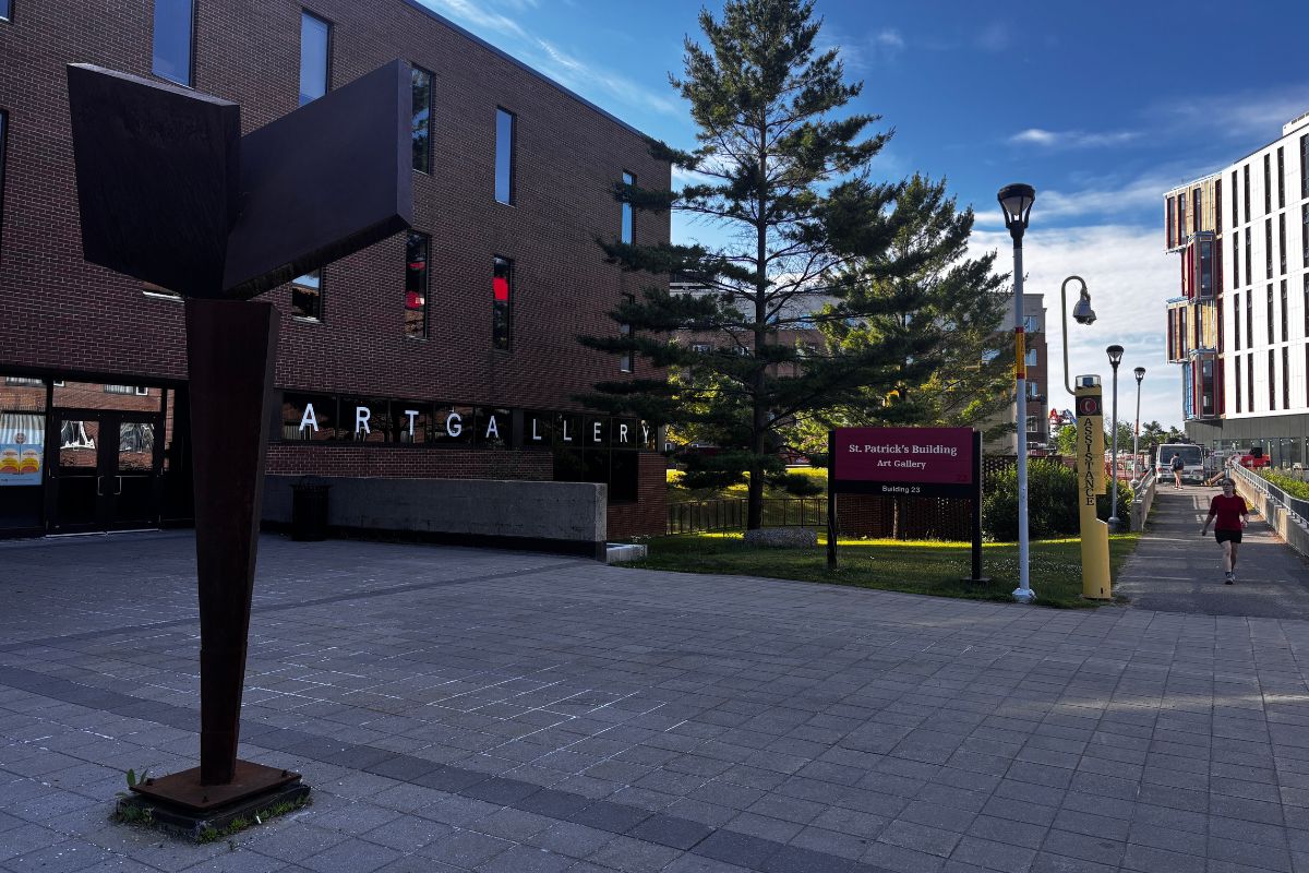 A tall gray statue stands in the middle of an open space by a sign that reads "St. Patrick's Building." 