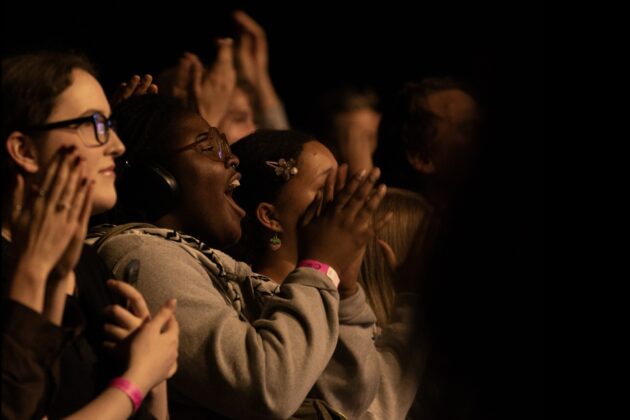 A crowd smiles and claps at night.