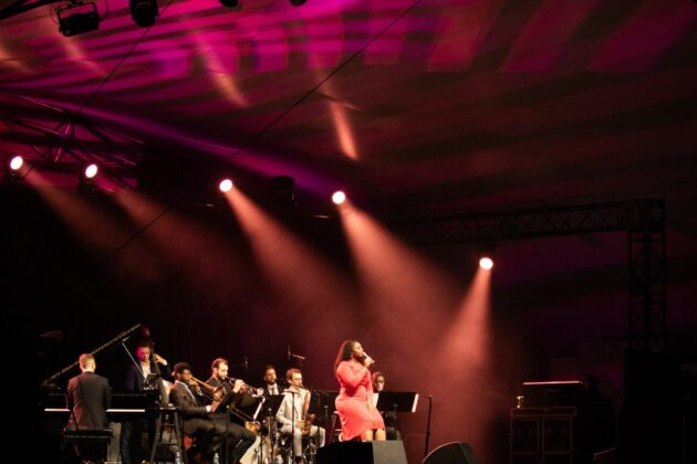 A band performs on stage under red lighting at night.