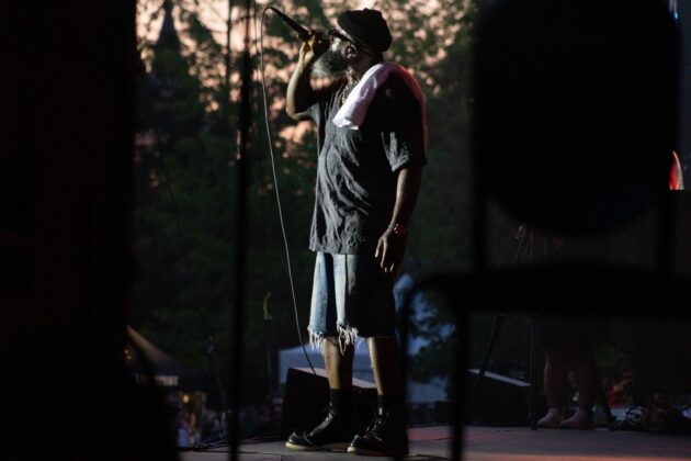 A person wearing all dark clothes sings into a microphone on a stage.
