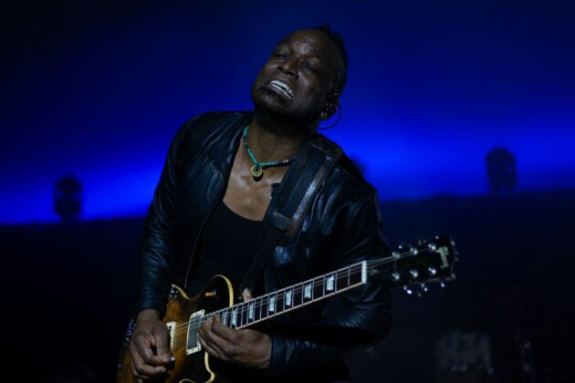 A guitar player plays passionately on a stage in blue lighting.