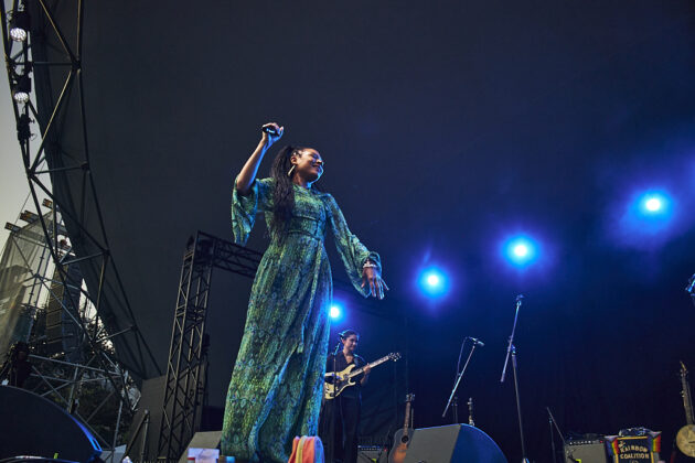 A woman dances on stage, smiling, in a green dress.