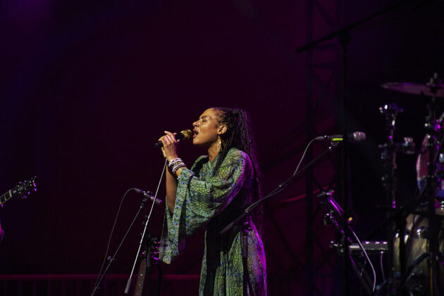A woman sings passionately on a stage with purple lighting.