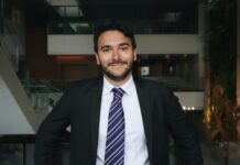 Q&A: Artur Estrela da Silva on ‘bridging gaps’ through advocacy and public service A person wearing a suit and tie stands and smiles, backdropped by a large space.