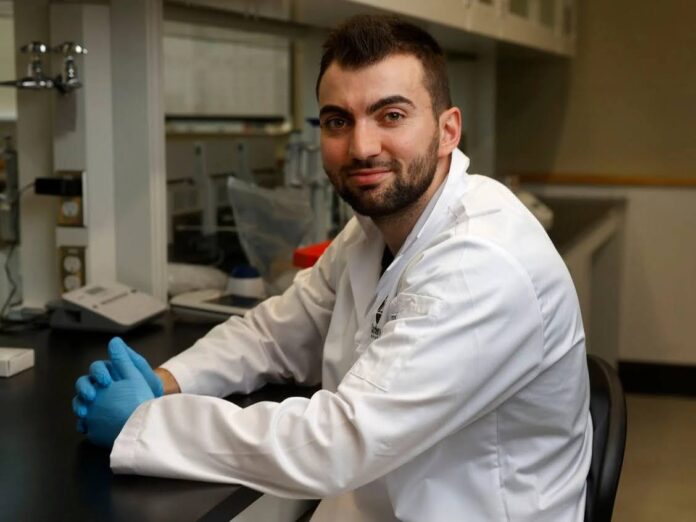 Man sitting down wearing a white lab coat.