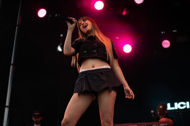 A woman sings on a stage under a pink spotlight.