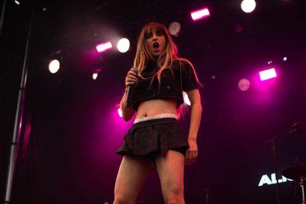A woman sings on a stage under a pink spotlight.
