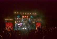 Bluesfest Day 5 review: Tom Morello, Def Leppard bring the protest, then the party A stage at night is lit up with projections in front of a clapping crowd.