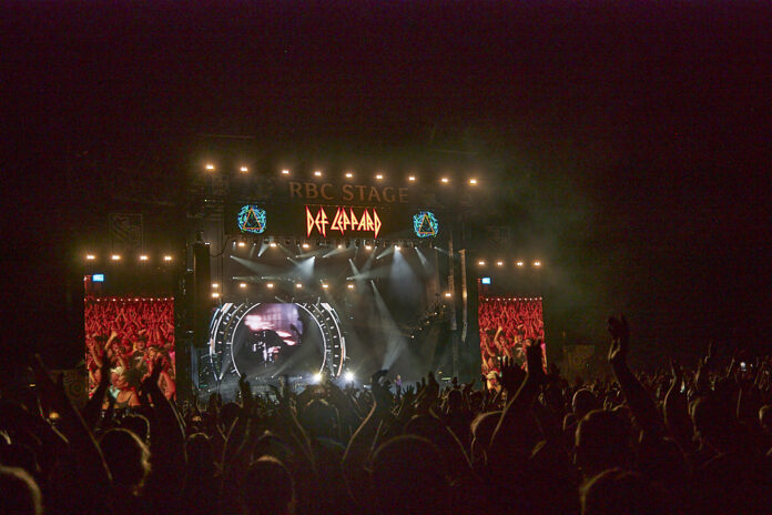 A stage at night is lit up with projections in front of a clapping crowd.