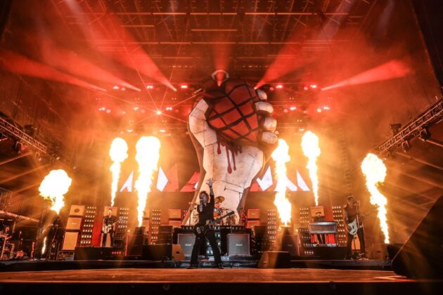 A band performs to a stage with red lighting and fire in the background.