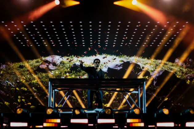 A DJ performs on a stage with spotlights and backdrops.