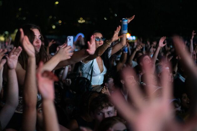 Crowds have fun at a concert, some are on friends' shoulders.