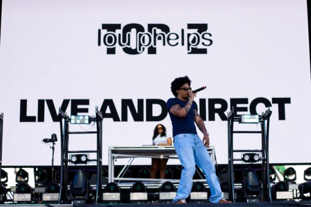 A rapper in light blue jeans performs on stage.